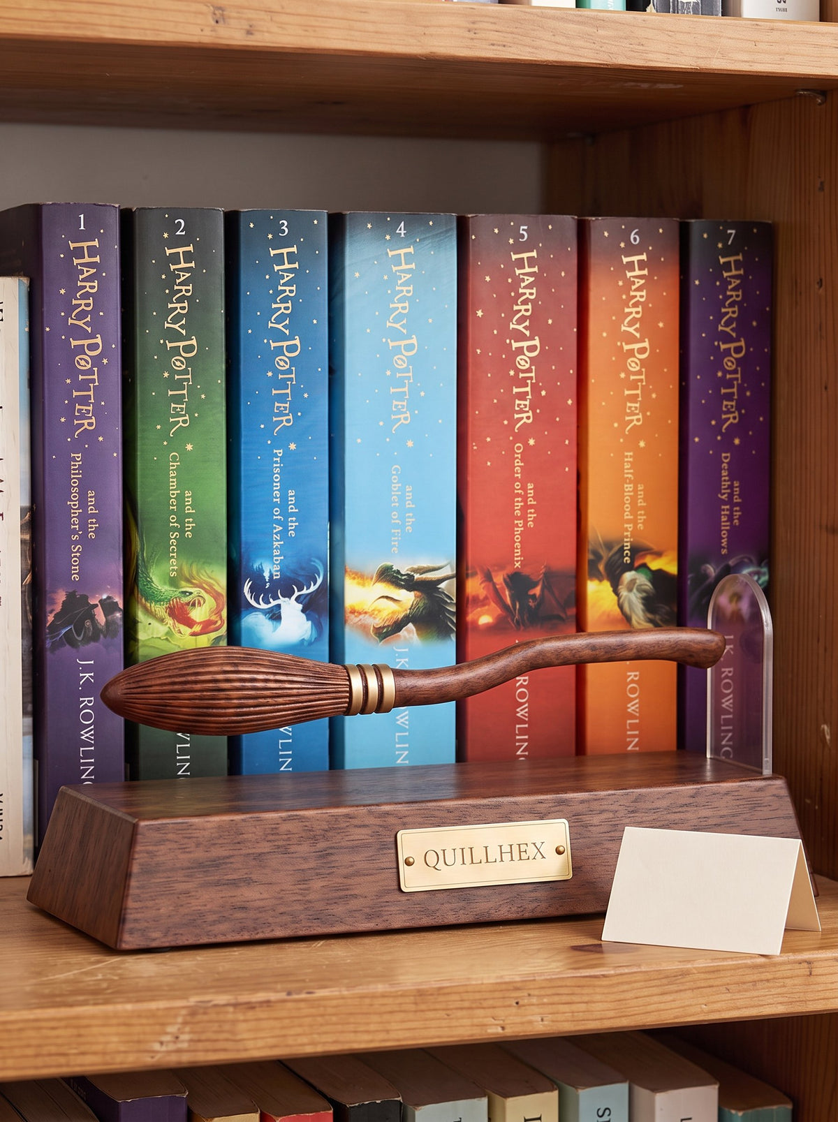 Quillhex magnetic broom pen levitating beside its rounded clear upright, with the seven-book Harry Potter collection on a real wooden bookshelf