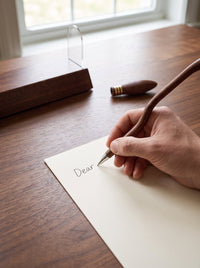Writing with the uncapped Quillhex broom pen on a clean walnut desk, with the removable cap beside it